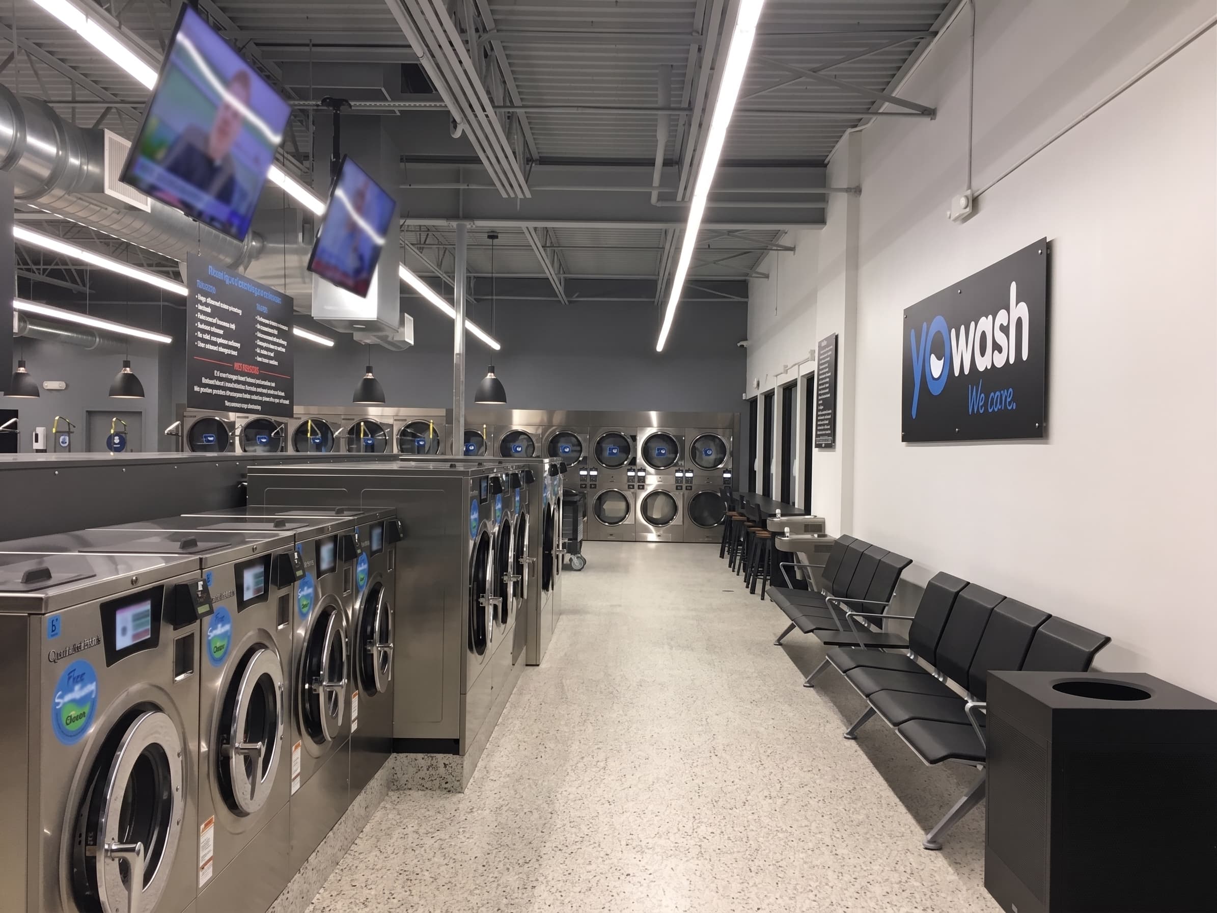 Inside YoWash Bradenton — rows of washers, dryers, smart TVs, and the YoWash 'we care' sign on the wall