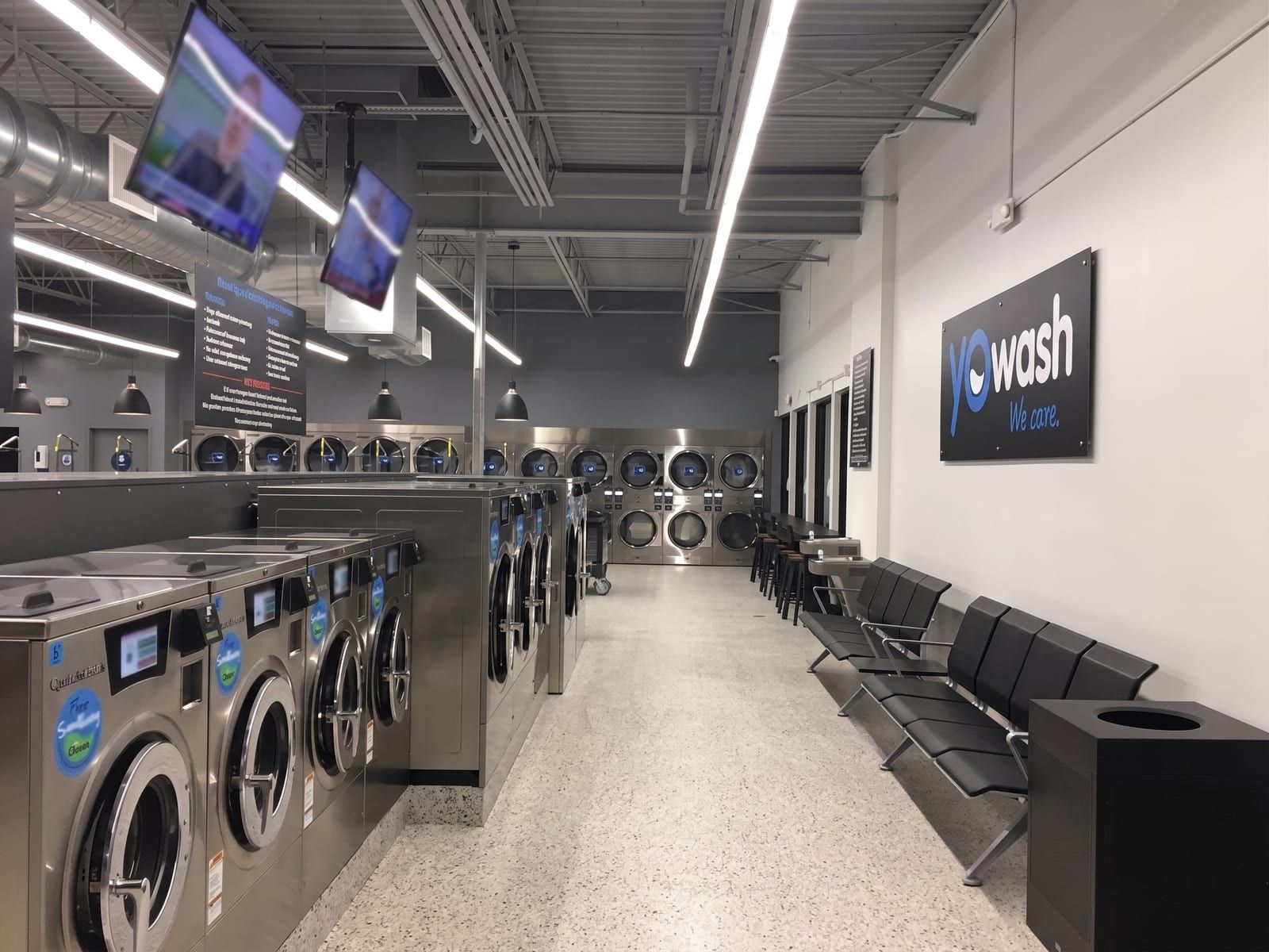 Inside YoWash Bradenton — rows of washers, dryers, smart TVs, and the YoWash 'we care' sign on the wall